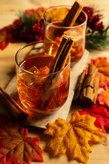 Top vertical view of two glasses of whiskey with ice cubes and cinnamon sticks on a wooden table, with mapple leaves and black background
