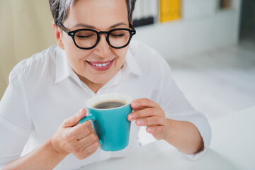 Closeup photo of beautiful elderly business owner broker woman senior holding blue cup cappuccino smell aromatic isolated office background