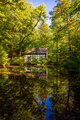 Obraz premium Idyllic small pond or artificial lake in the public forest of Iserlohn Germany. Reservoir with pump station and reflection for water supply on a sunny summer evening in fresh green Sauerland scenery.