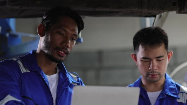 Two mechanics in a car repair shop are discussing repairs to the underbody and suspension of an old car. Auto mechanic is checking the engine's operating system.