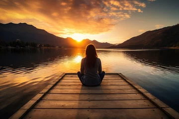Foto op Plexiglas woman sits on jetty at peaceful lake at sunset © krissikunterbunt