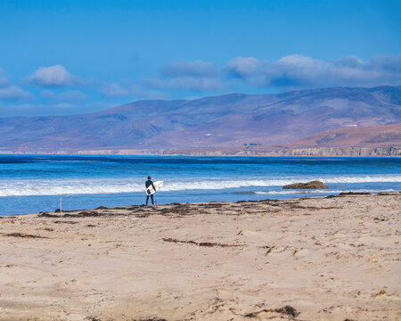 Lompoc, CA, USA – September 18, 2023: A man prepares to enter the Pacific ocean to surf at Jalama Beach in Lompoc, CA.