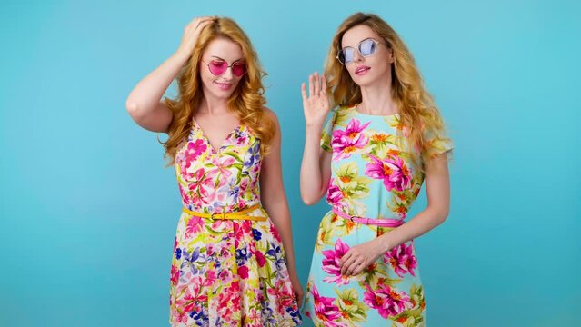 Friends, woman showing handshake gesture, hello hi, smiling friendly, invite. Two women sister exited greeting and welcoming, wave hand in trendy outfit, friendly laughing. Studio blue background.