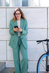 Business woman standing on stairs outside office building while using her cellphone next to a bike