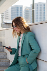 Business woman standing on stairs outside office building while using her cellphone