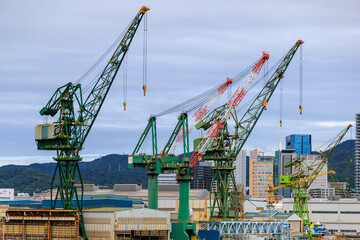 Fototapeta na wymiar Loading cranes and city buildings by industrial port