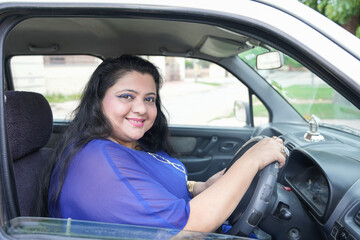 Happy plus size indian woman sitting in car without wearing seat belt looking at camera with smile ready to drive.