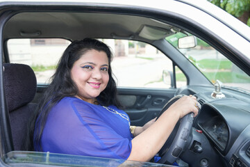 Fototapeta premium Happy plus size indian woman sitting in car without wearing seat belt looking at camera with smile ready to drive.