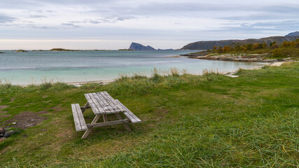 Seating area at Sommar&oslash;ya beach, BBQ area on the shore of the North Atlantic, in Troms, Norway. wooden park bench with table, Dining table with attached seats on meadow, outdoor area on the seashore