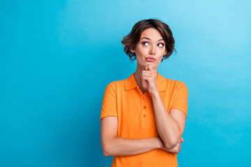 Photo of doubtful unsure lady wear orange t-shirt arm chin looking empty space isolated blue color background