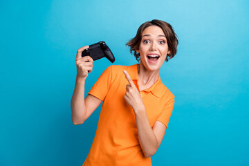 Photo of cheerful lucky girl dressed orange polo pointing finger playstation isolated blue color background