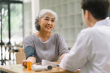 A young doctor using digital tonometer check blood pressure for senior woman. A doctor is holding a senior woman's hand.