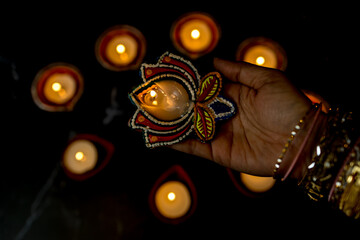 Happy Diwali - Woman hands with henna holding lit candle isolated on dark background.