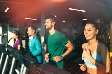 Side view of athletic people running on treadmills in a gym. Group of exhausted young friends doing...