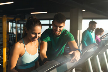 Fototapeta na wymiar Young athlete male assisting a young woman while exercising on treadmills in a gym. Fitness instructor giving instructions to his client.