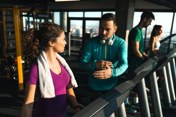 Group of athletic people talking while running on treadmills in a gym. Professional athlete giving...