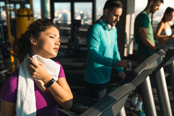 Exhausted athletic woman wiping  sweat from neck on a break after running on a treadmill. Attractive woman feeling tired after intense cardio training.