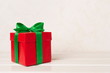 Red gift box with green ribbon and bow on table
