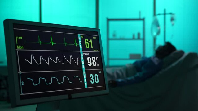 Close-up video capturing intencive care unit showing heart and pressure rate. Blurred silhouette of a patient laying in bed on the background. He is connected to breathing support.