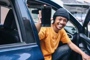 Smiling online taxi driver showing blank phone screen for mockup while sitting in car