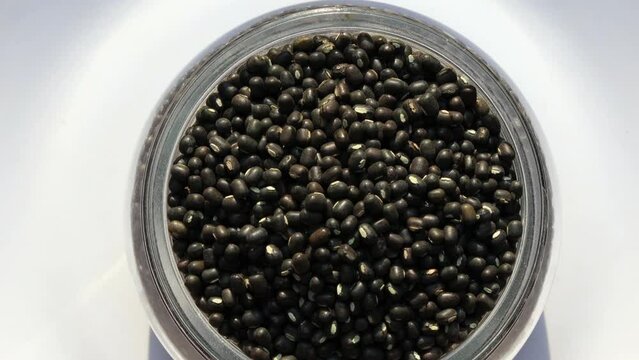 Black Lentil or masoor dal filled in glass bowl table top spin isolated on white background.
