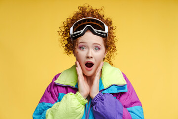 Excited attractive curly woman wearing protective ski goggles ski overalls, looking at camera