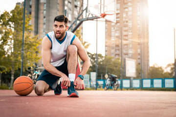 Basketball player tying shoelace for game at basketball court outdoors. Male basketball athlete getting ready to play sport in urban city neighborhood.