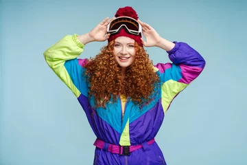 Fotobehang Smiling girl wearing stylish ski overalls, ski goggles, looking at camera. Winter travel concept © Maria Vitkovska