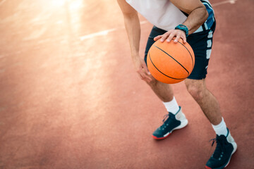 Naklejka premium Sportsman playing basketball at basketball court outdoors. Photo of unrecognizable male person in movement dribbling a ball through playground. Focus on basketball.