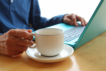 Closeup of a cup of coffee with a man working on laptop in the backdrop