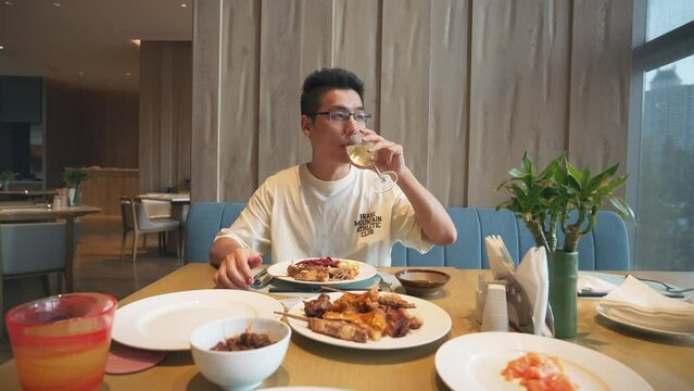 An Asian man drinks a drink while eating