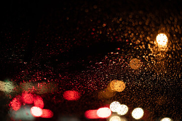 Rain drops on the car glass with traffic light bokeh background.