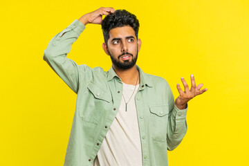 I don't know what to say. Confused Indian young man feeling embarrassed about ambiguous question, having doubts, no answer, idea, being clueless, uncertain. Guy isolated on yellow studio background - obrazy, fototapety, plakaty