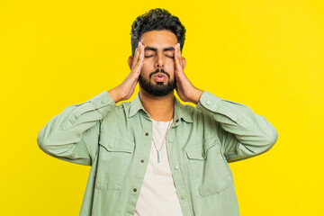 Displeased exhausted Indian Hindu man guy rubbing temples to cure headache problem, suffering from tension, migraine, stress, grimacing in pain, high blood pressure isolated alone on yellow background