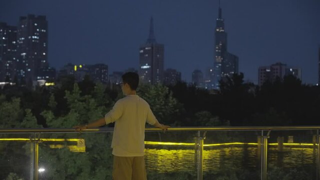An Asian man watches the city night view from the balcony