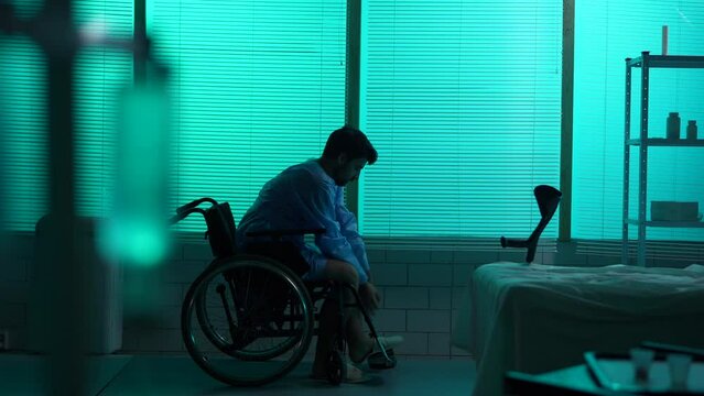 Full-sized silhouette video of a disabled man, patient with mobility impairment trying to get up from a wheelchair, making a few succesful steps leaning on a crutch.