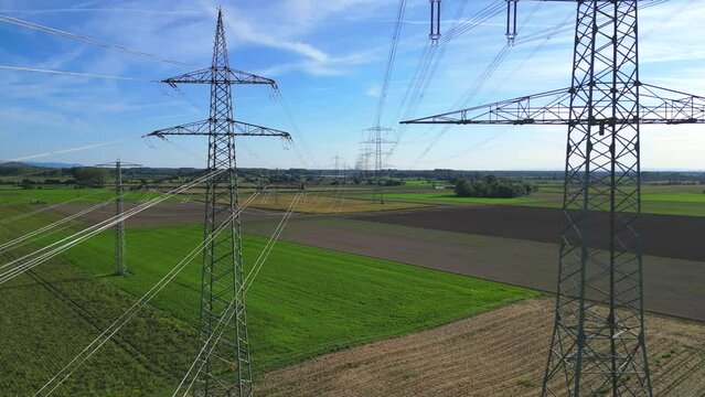 Flug mit einer Drohne durch zwei Hochspannungsmasten mit Stromleitungen &uuml;ber landwirtschaftlichen Feldern