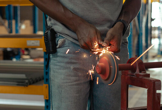 Hombre afro de piel morena usa un esmeril para limar acero con chispas