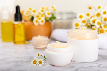 Fototapeta na wymiar Chamomile spa. Composition with chamomile flowers, handmade soap, essential oil cosmetic bottle, body cream, scrub and sea salt on a white texture background. Relaxing beauty treatments.Copy space