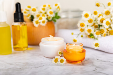Chamomile spa. Composition with chamomile flowers, handmade soap, essential oil cosmetic bottle, body cream, scrub and sea salt on a white texture background. Relaxing beauty treatments.Copy space
