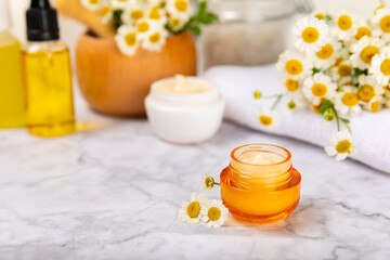 Chamomile spa. Composition with chamomile flowers, handmade soap, essential oil cosmetic bottle, body cream, scrub and sea salt on a white texture background. Relaxing beauty treatments.Copy space