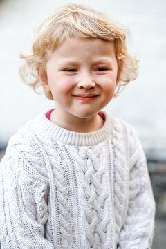 Portrait of a smiling blonde girl on a light wall background. Child in white knitted sweater