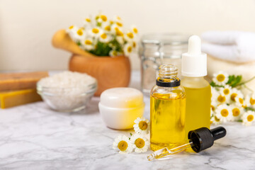 Chamomile spa. Composition with chamomile flowers, handmade soap, essential oil cosmetic bottle, body cream, scrub and sea salt on a white texture background. Relaxing beauty treatments.Copy space