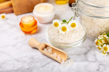 Chamomile spa. Composition with chamomile flowers, handmade soap, essential oil cosmetic bottle, body cream, scrub and sea salt on a white texture background. Relaxing beauty treatments.Copy space