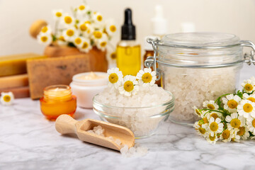 Chamomile spa. Composition with chamomile flowers, handmade soap, essential oil cosmetic bottle, body cream, scrub and sea salt on a white texture background. Relaxing beauty treatments.Copy space