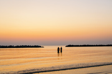 two figures walk on the sea at dawn