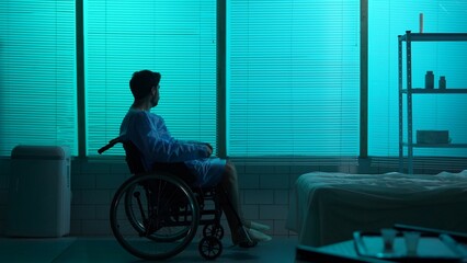 Full-sized silhouette shot of a disabled man, patient with mobility impairment entering the frame on a wheelchair, looking at the window sorrowfully.