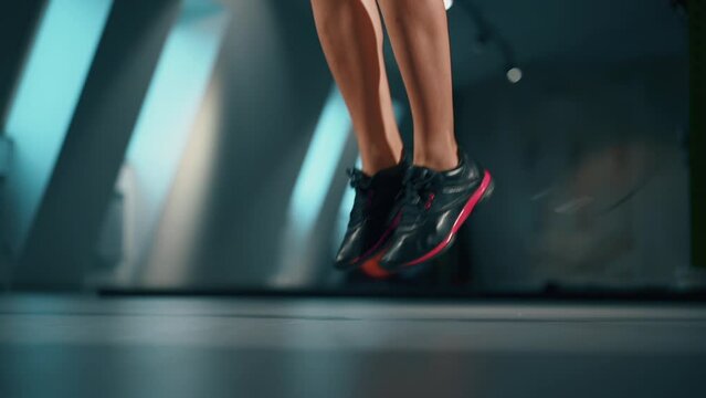 woman faceless feet in snickers shoes using jumping rope in dark gym. Sports exercises. Girl working on healthier body. Sport active lifestyle, beauty and wellness concept. Closeup details. Lonely