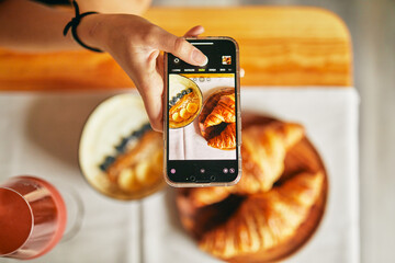 Person capturing croissants and red drink with smartphone. Casual breakfast setup with emphasis on...