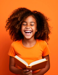 Portrait of a cute little african american girl laughing while reading a book on orange background